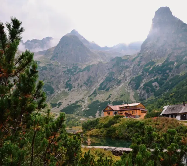 Słowackie Tatry: schroniska nad jeziorem, otoczone zielenią i majestatycznymi szczytami, z mgłą unoszącą się w tle.