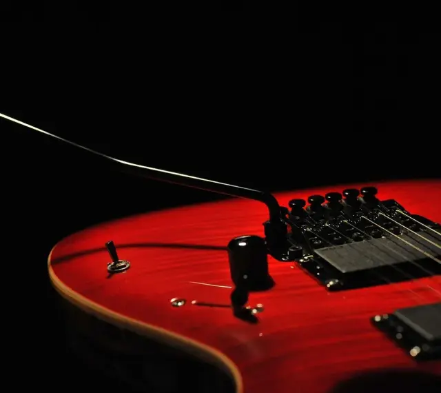 Czerwona gitara elektryczna z czarnym mostkiem tremolo, gotowa do wydobycia dźwięków, które poruszą serce.