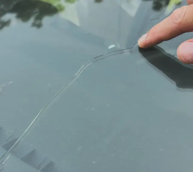 Palec wskazujący na pękniętej szybie samochodowej. Sprawdź autoglass cennik, aby poznać koszt naprawy.