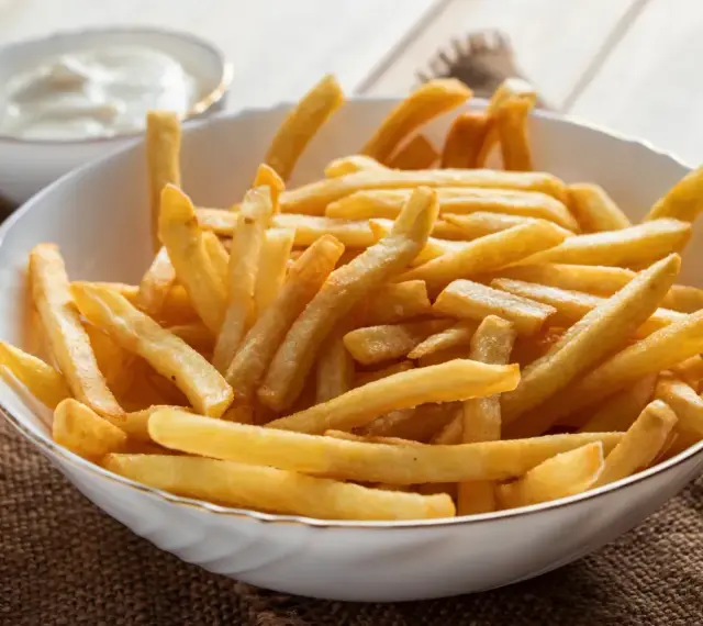 Chrupiące frytki z airfryer w białej misce, obok sos. Idealna przekąska na każdy dzień.