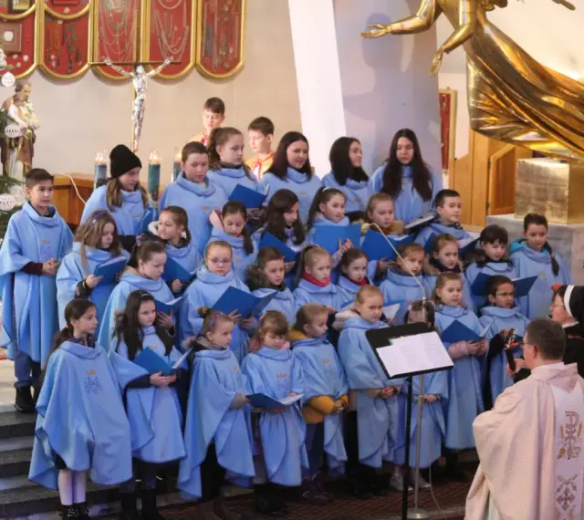 Dzieci w błękitnych strojach tworzą schola, śpiewając w kościele przy choince.