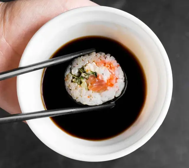 Pałeczkami zanurzam sushi w sosie do sajgonek. Widać kawałek łososia i ryż.