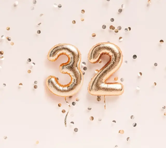 Złote balony z cyframi 3 i 2, otoczone konfetti. To już 32 tydzień ciąży, który to miesiąc?
