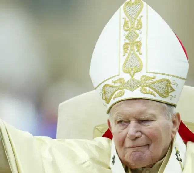 Papież Jan Paweł II w białej mitrze z haftem, pozdrawia wiernych. Jego dłoń z pierścieniem jest uniesiona. Codzienna modlitwa do św. Jana Pawła II.