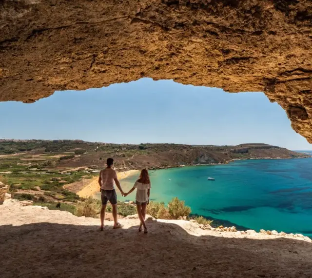 Para w jaskini podziwia widok na turkusowe morze i plażę. Malta pogoda wrzesień idealna na wakacje.