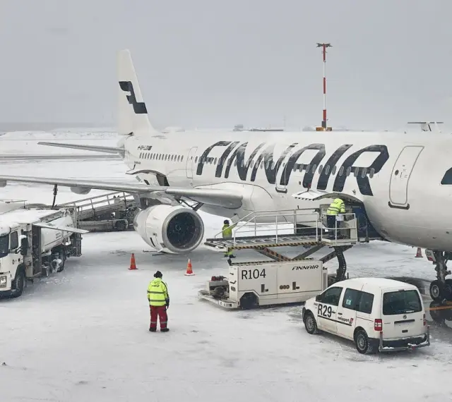 Samolot Finnair na lotnisku w śnieżny dzień. Pracownicy obsługi naziemnej przygotowują samolot do lotu. Czy do Finlandii można lecieć na dowód?