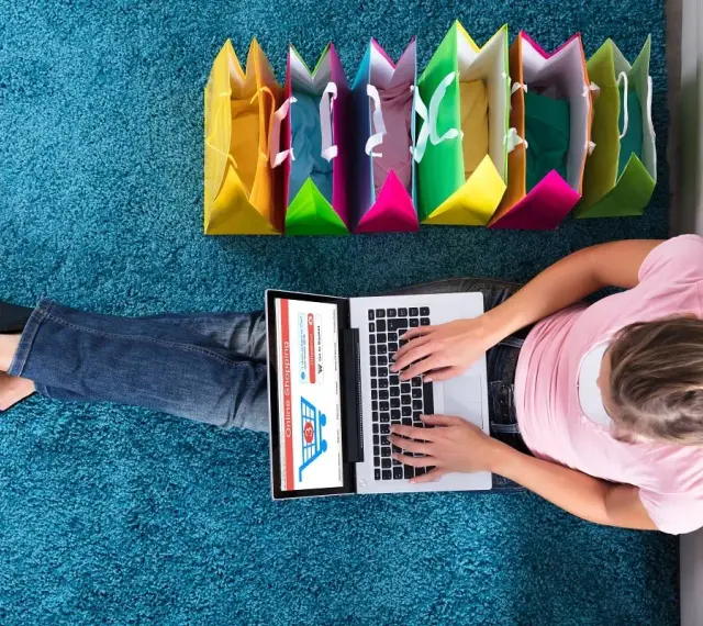 Kobieta robi zakupy online, obok kolorowe torby. To idealny sposób na zakupy z **Deezee firma**.