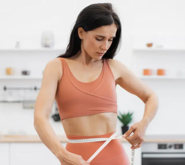 Kobieta w sportowym stroju mierzy talię, ciesząc się efektami diety low carb.
