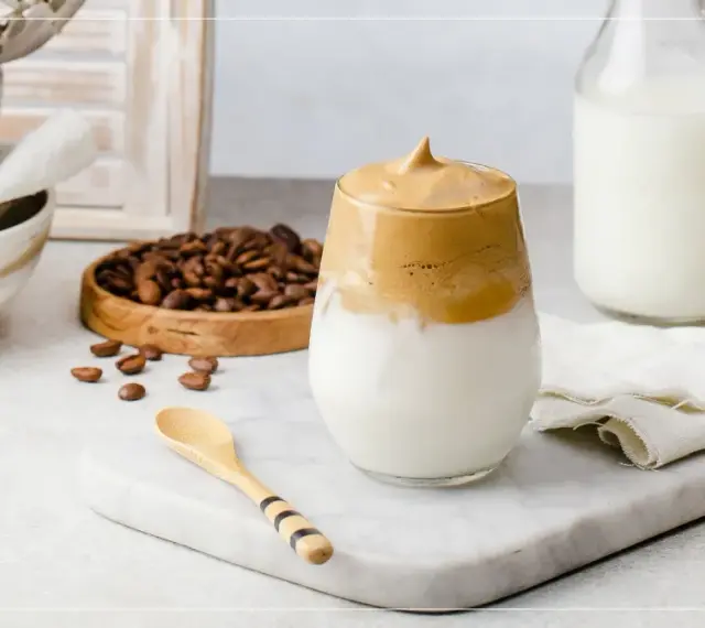 En krämig dalgona coffee med fluffigt skum, serverad med mjölk och kaffebönor.