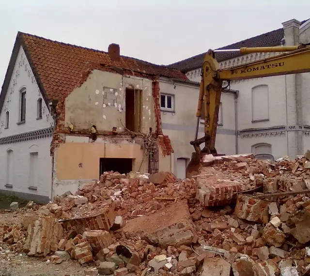 Rozbiórka budynku w granicy działki. Koparka Komatsu pracuje przy gruzach.