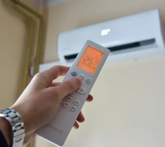Dłoń trzymająca pilot do klimatyzacji, ustawiona na 25°C. Kontroluj komfort i miesięczny koszt klimatyzacji.