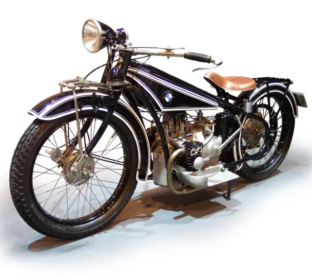 Klasyczny motocykl BMW z lat 20. XX wieku, czarny z białymi pasami, z brązowym siodłem. Ikona historii BMW.
