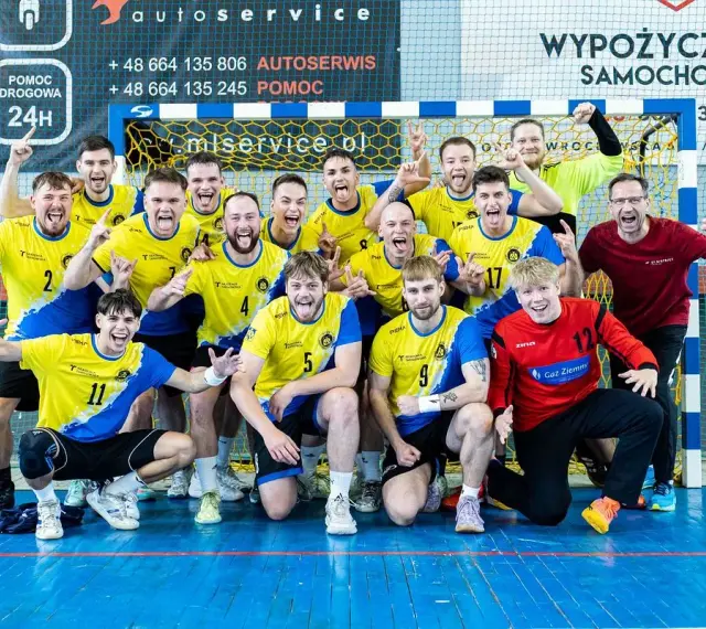 Drużyna Unii Tarnów piłka ręczna świętuje zwycięstwo. Radośni zawodnicy w żółto-niebieskich strojach pozują do wspólnego zdjęcia.