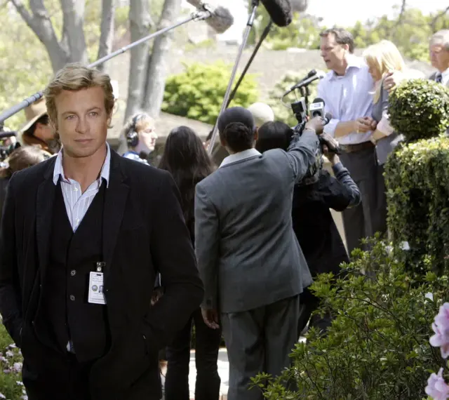 Simon Baker, con la sua nuova fidanzata, è circondato da telecamere e microfoni durante un evento all'aperto.