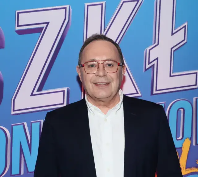 Uśmiechnięty mężczyzna w okularach na tle napisu "SZKŁO KONTAKTOWE OBSADA".
