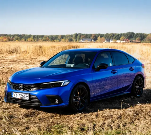 Błękitny Honda Civic 11. generacji na tle jesiennego pola.