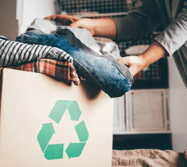 Pudełko z ubraniami i symbolem recyklingu. Wiesz, gdzie można oddać ubrania za darmo?