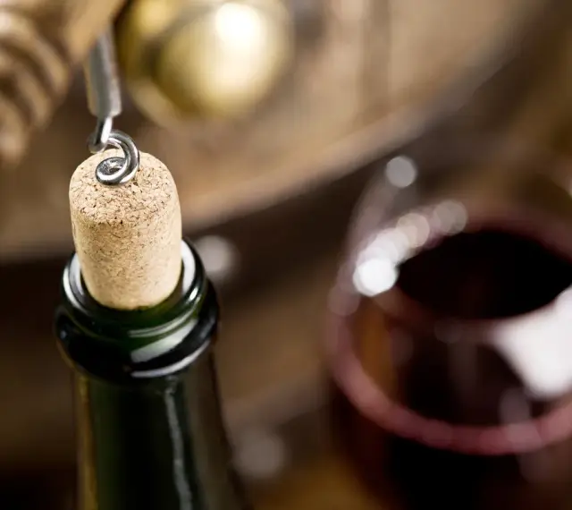 Korek wyciągany z butelki wina, kieliszek czerwonego wina i beczka. Czy wino ma datę ważności? To pytanie zadaje sobie wielu miłośników tego trunku.