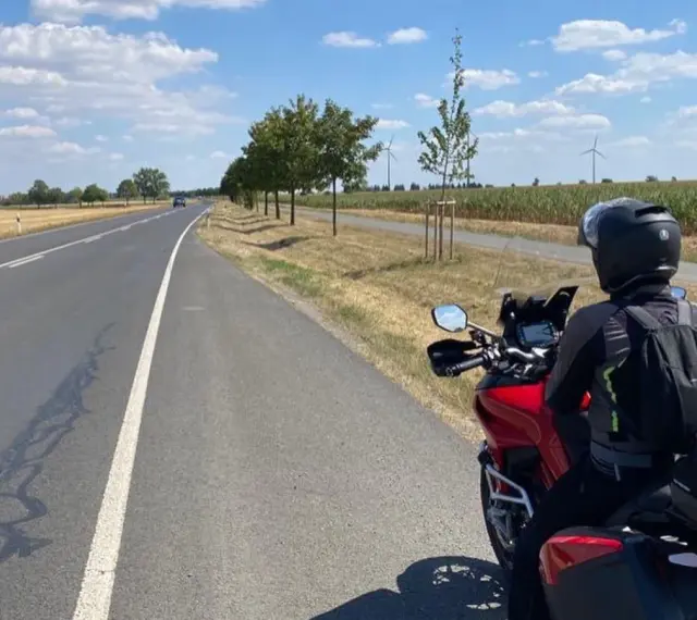 Motociclista su strada panoramica Foresta Nera, con campi di mais e pale eoliche all'orizzonte.