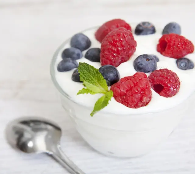 Pyszny jogurt z malinami i borówkami, idealny na śniadanie lub jako element diety jogurtowej. Obok leży łyżeczka.