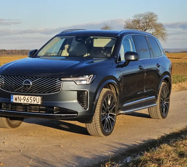 Ciemnoszary Volvo XC90 T8 na tle jesiennego krajobrazu. Elegancki SUV z nowoczesnym grillem i światłami LED.