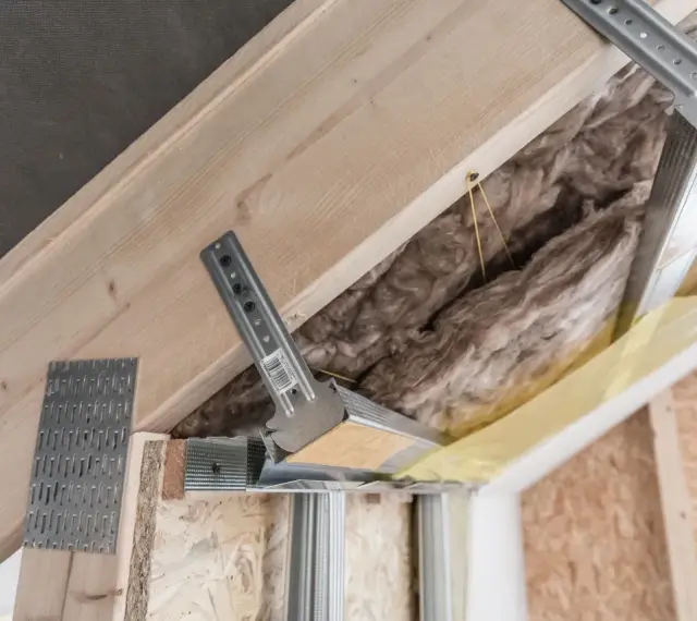 Konstrukcja poddasza z wełną mineralną i metalowymi wieszakami kotwowymi, gotowa do montażu płyt gipsowo-kartonowych.