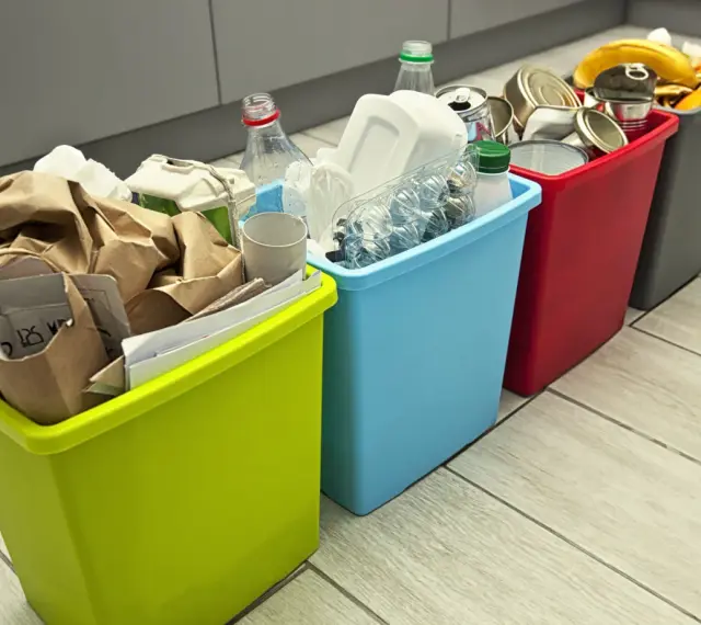 Cztery kolorowe kosze na śmieci z posegregowanymi odpadami: papier, plastik, metal i bio.