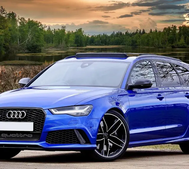Niebieski **hatchback** z napędem quattro, zaparkowany nad jeziorem, z pięknym zachodem słońca w tle.