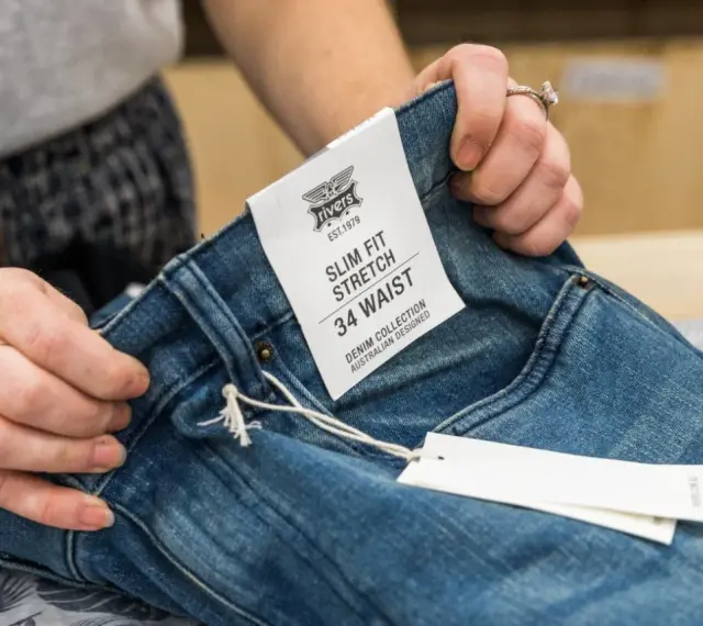 Dłonie trzymają dżinsy z metką "SLIM FIT STRETCH 34 WAIST". Czy to dobry rozmiar?