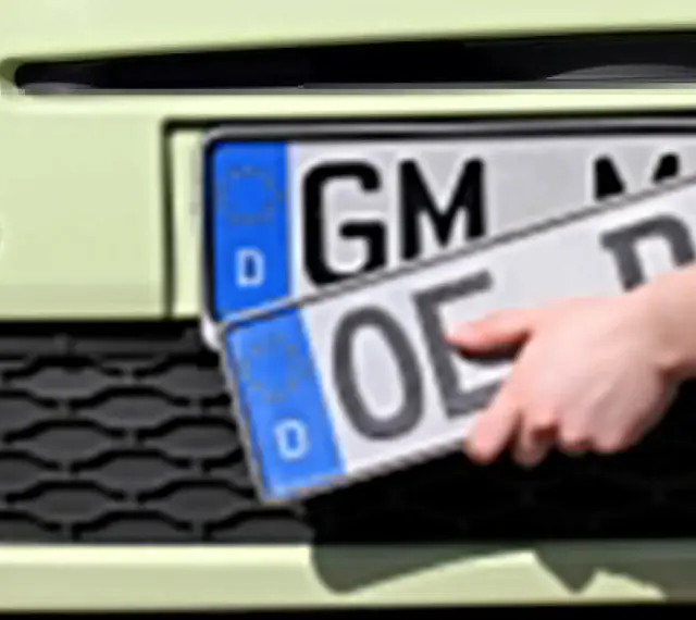 Dłoń trzyma niemieckie tablice rejestracyjne z literami "OE" i "GM".
