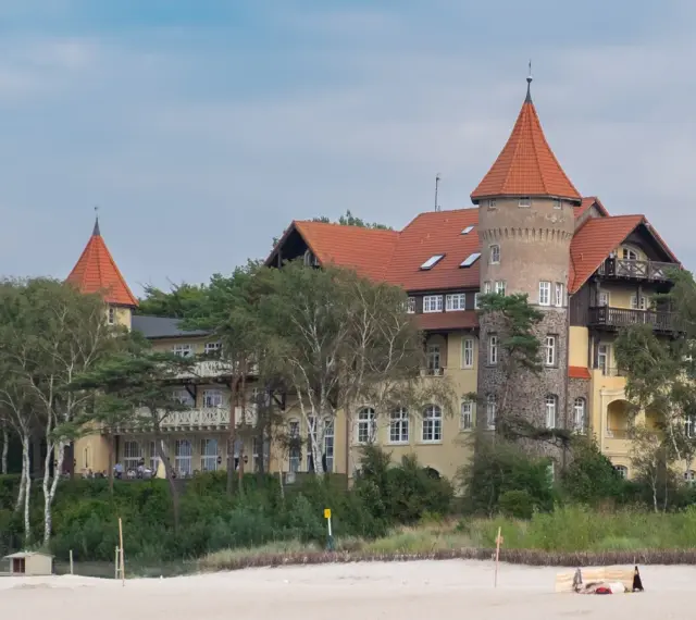 Elegancki hotel z wieżą i czerwonym dachem, otoczony drzewami, idealny na łeba atrakcje dla dorosłych.