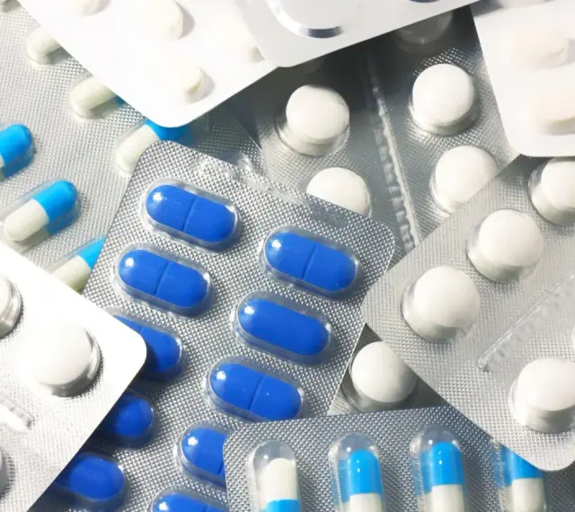Blistry z białymi i niebiesko-białymi kapsułkami oraz białe tabletki. Wśród nich można znaleźć polopirynę, która pomaga złagodzić ból i gorączkę.
