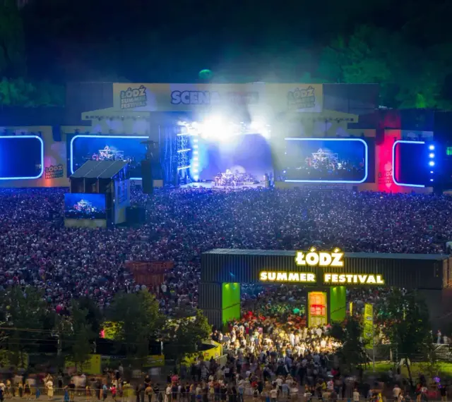 Tłum ludzi na koncercie podczas Łódź Summer Festival 2026. Na scenie gra zespół, a widzowie oświetlają teren telefonami.