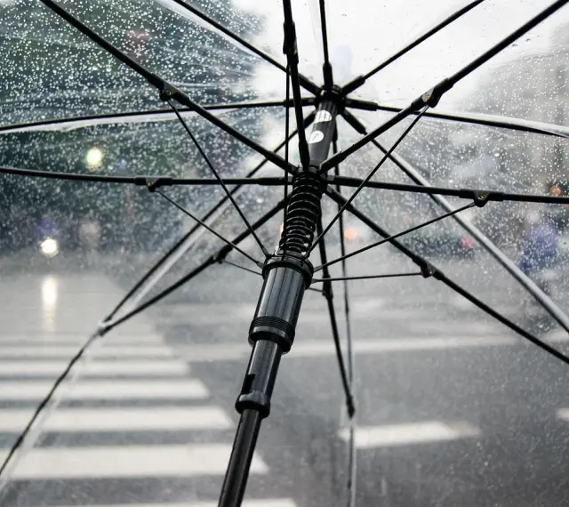 Przezroczysty parasol w bagażu podręcznym chroni przed deszczem na ulicy. Krople wody na materiale.
