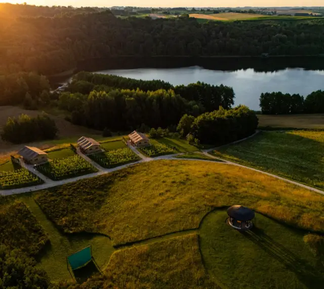 Idealne miejsce, gdzie pojechać na weekend: urokliwe domki nad jeziorem, otoczone zielenią i polami, w złotym świetle zachodzącego słońca.