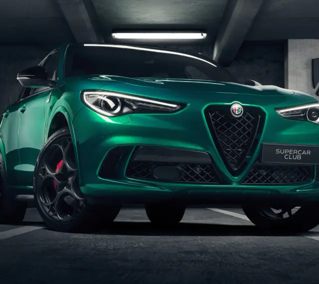 Zielony Alfa Romeo Stelvio Quadrifoglio z czarnymi felgami i czerwonymi zaciskami hamulcowymi, zaparkowany w garażu.