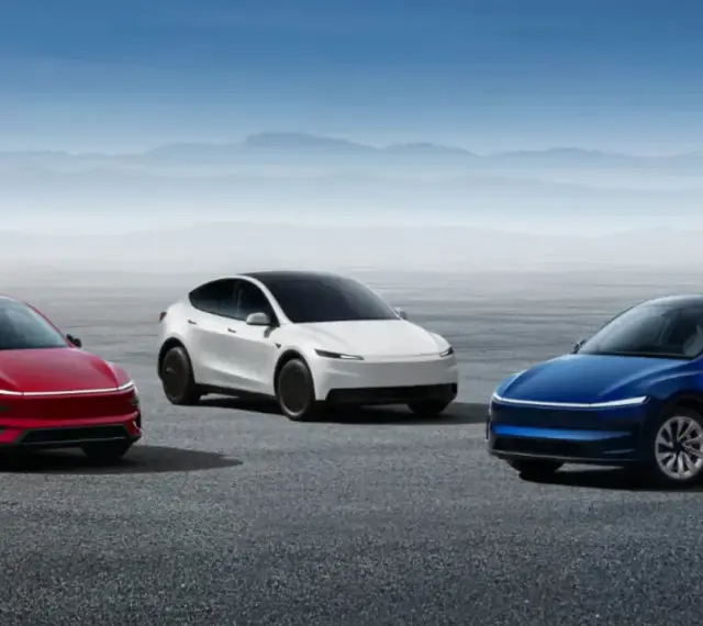 Trzy samochody Tesla: czerwony, biały i niebieski, stoją na pustkowiu pod błękitnym niebem.