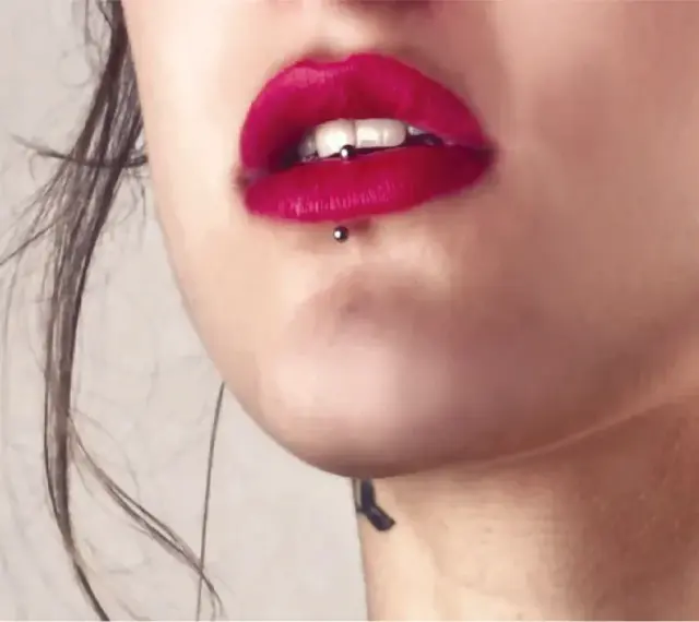 Usta z czerwoną szminką i ashley piercing. Delikatny tatuaż na szyi dodaje uroku.
