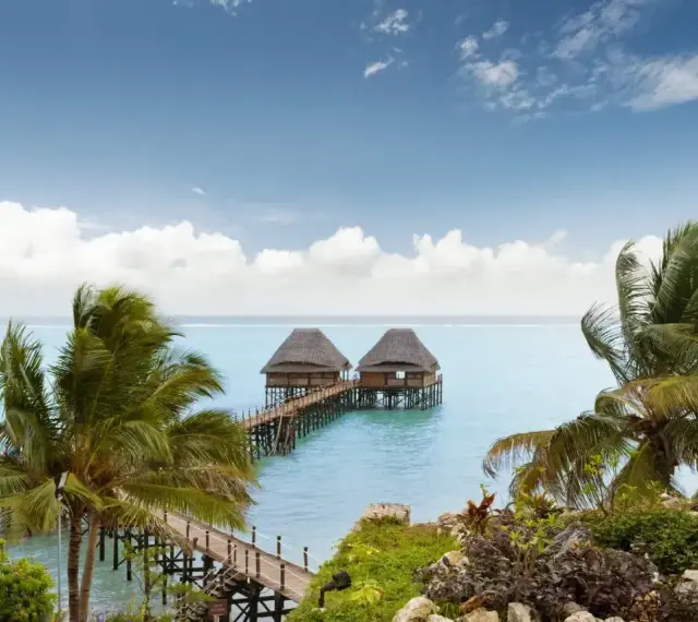 Dwa domki na wodzie z palmami w tle, idealne na spokojny wypoczynek podczas pory deszczowej na Zanzibarze.