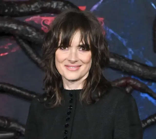 Winona Ryder, gwiazda filmów i seriali, w tym "Stranger Things", na tle dekoracji z mackami i logo Netflix.