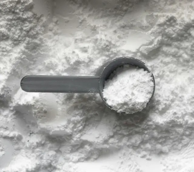 Miarka z białym proszkiem, prawdopodobnie disodium edta, na tle sypkiego materiału.