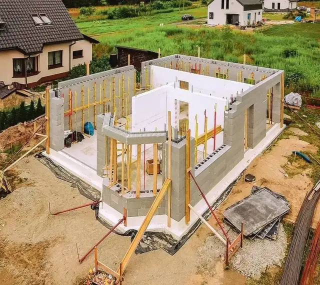 Budowa domu ze styropianu w toku. Ściany z bloczków betonowych i białego styropianu, zbrojenia i drewniane podpory.