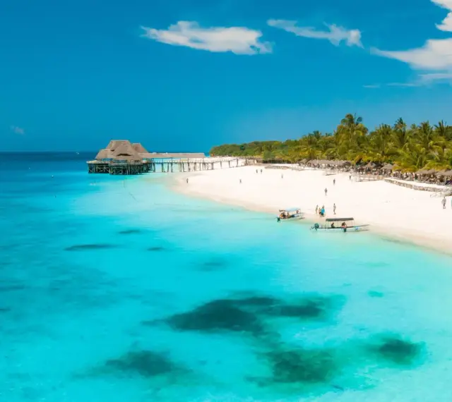Rajskie plaże Zanzibaru w lutym. Turkusowa woda, biały piasek, palmy i urokliwy pomost z domkami na wodzie.