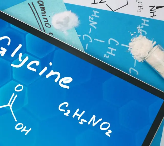 Tablet z napisem "Glycine", wzorem chemicznym i próbówką z proszkiem. Informacje o glicynie i jej dawkowanie.