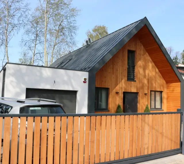 Nowoczesny dom z drewnianą dobudówką do części murowanej. Obok garaż, przed którym stoi samochód.