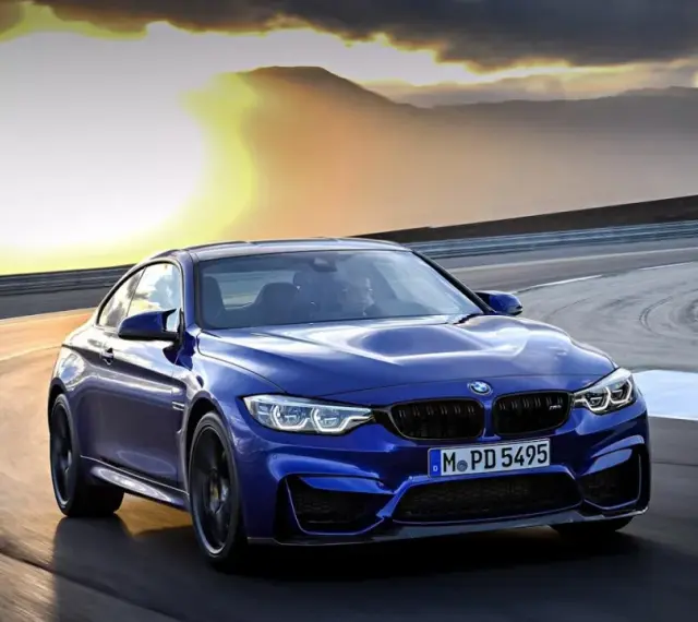 Niebieskie BMW M2 CS pędzi po torze wyścigowym podczas zachodu słońca.