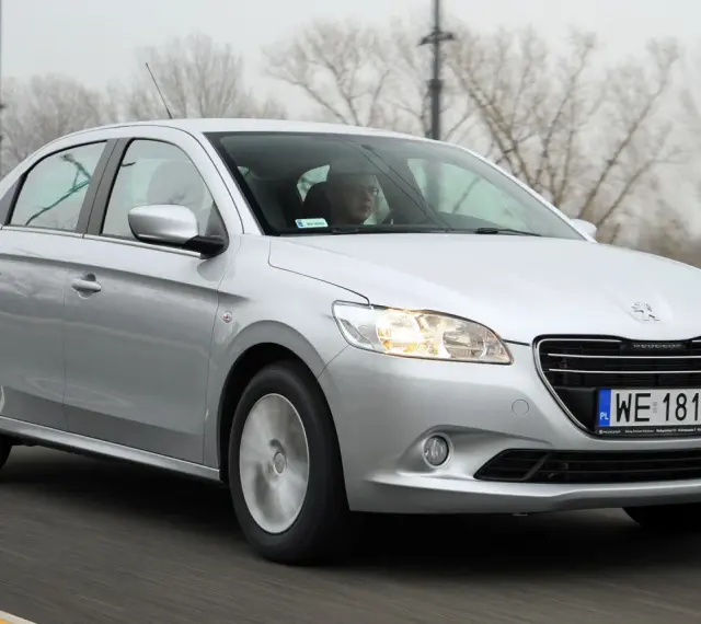 Srebrny Peugeot 301 jedzie po drodze, za kierownicą siedzi mężczyzna w okularach.