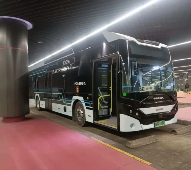 Nowoczesny, czarny autobus elektryczny z napisem "100% ELEKTRYCZNY" stoi na przystanku.
