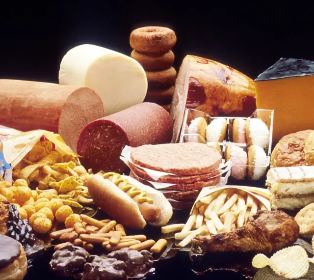 Stół ugina się pod ciężarem przetworzonej żywności: wędliny, sery, frytki, słodycze, ciastka, pączki, hamburgery i chipsy – to wszystko zawiera tłuszcze trans.