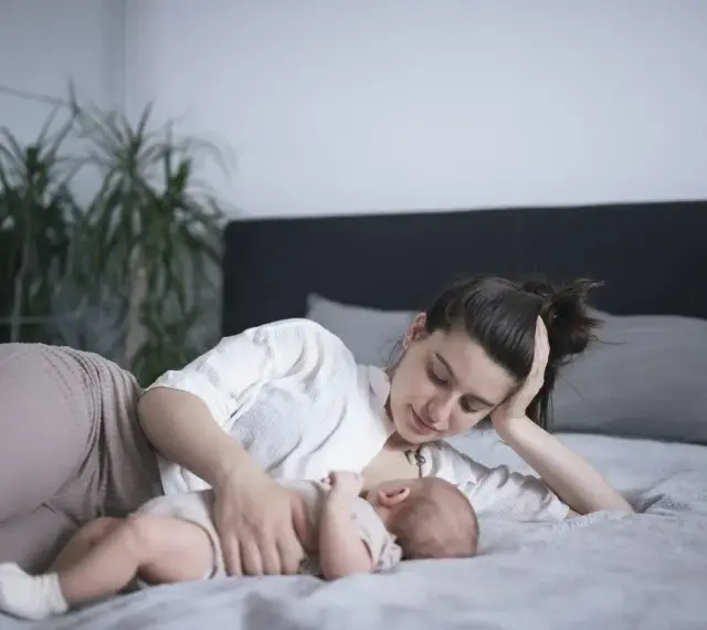 Matka karmi piersią dziecko na leżąco, opierając głowę na dłoni. Czuły moment bliskości.